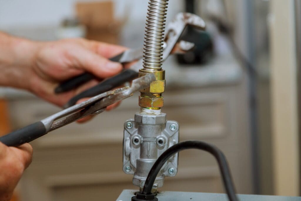A person tightens a flexible metal gas pipe connection on a gas appliance with two wrenches, demonstrating essential plumbing repairs for tankless water heaters.